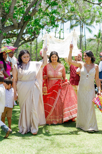 Two people walking in front of a newlywed as they walk down the aisle 