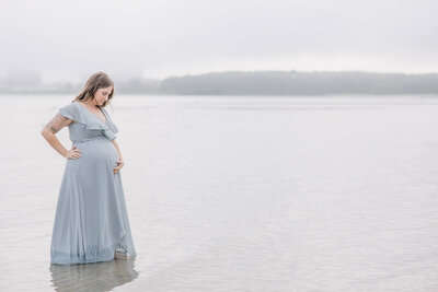Pregnant woman in light blue dress looks down at her belly.