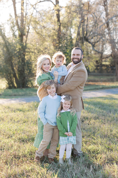Woman in green dress stands with husband in tan suit jacket holding three children in field