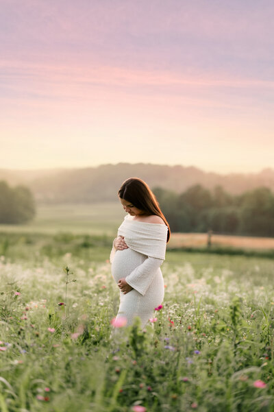 pregnant woman in white dress standing in a wildflower meadow at sunset near Harrisburg, PA