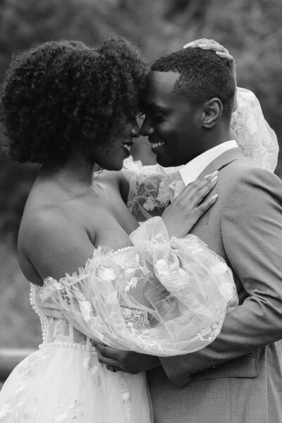 A Black couple smiles at each other and embraces in their wedding clothes