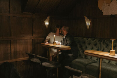 Couple kissing in a moody-lit back booth at a bar during an intimate session