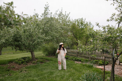 woman standing in backyard cottage garden surrounded by greenery and soft spring blooms

