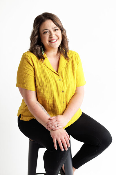 Headshot of woman in yellow shirt sitting on stool white background personal branding