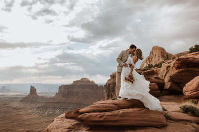 bride and groom standing on a large rock formation with the desert in the background