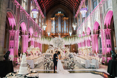 A bride and groom share a kiss in front of their opulent wedding reception decor at Trinity Cathedral
