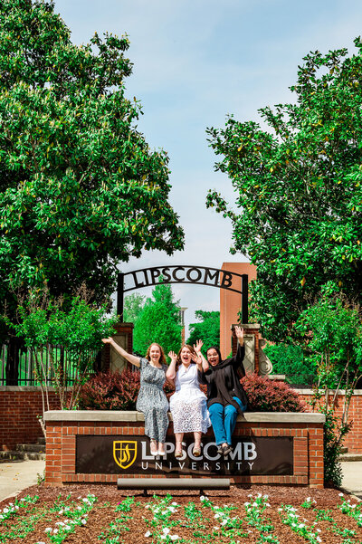 Three friends are sitting on the Lipscomb sign with the arbor behind them