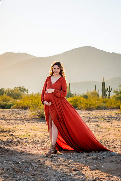 expecting mother walking powerfully through the Arizona desert while holding baby bump. 