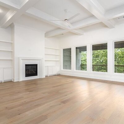 A spacious living room with big windows, vaulted ceilings, and new hardwood flooring.