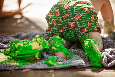 A baby in a green outfit joyfully playing with a cake during a cake smash session in Orlando.