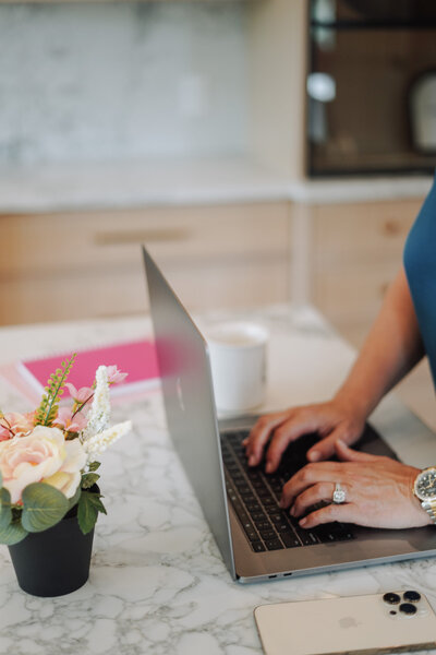 Woman's hands typing on a laptop next to a vase of flowers