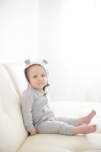 baby wearing a bear ear hat sitting on sofa at Tiffany Hix Photography studio in Boise