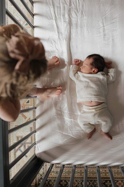A newborn sleeps peacefully in a crib while a sibling looks on, showcasing the natural charm of Cleveland lifestyle newborn photography.