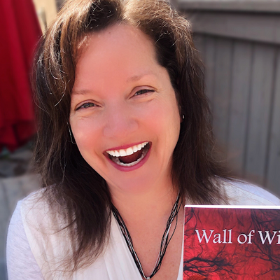 Suzy, a white woman with shoulder-length brown hair grins and holds up a book