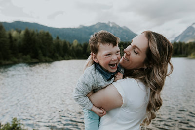 mother holding laughing son at mountain lake