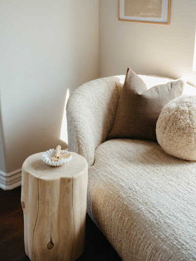 Textured neutral accent chair with boucle pillow and wood stump side table in a sunlit corner, styled by San Diego interior designer Natalie Barnas.