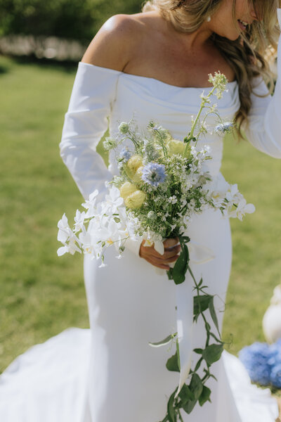 bride holding a beautiful bouquet of white roses, with her lace wedding dress and veil partially visible