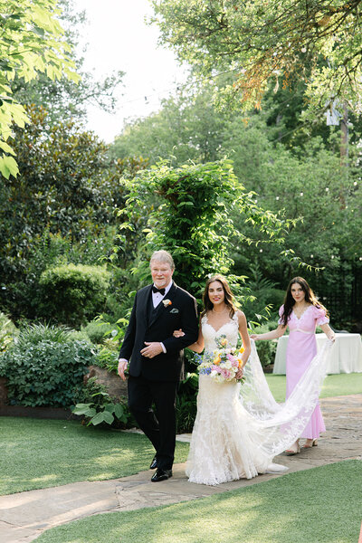 The bride is escorted to the ceremony site through the gardens at Hummingbird House in Austin.