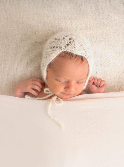 A newborn baby sleeps peacefully under a blanket with a knitted bonnet cap