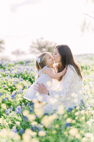 Mother kissing her 1 year old daughter in a field of bluebonnets.