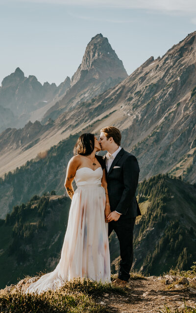 a stunning shot of a couple in their wedding attire embracing in front of a jagged mountain range. Golden light shines on them creating a dreamy quality as their adventure elopement photographers document this moment. 