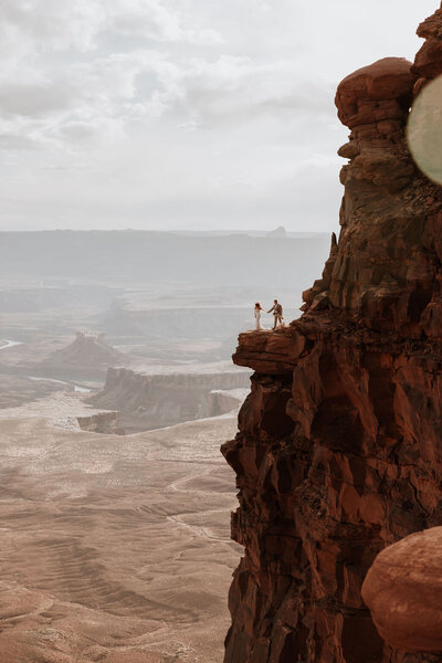 bride and groom standing on a cliff with the desert below them