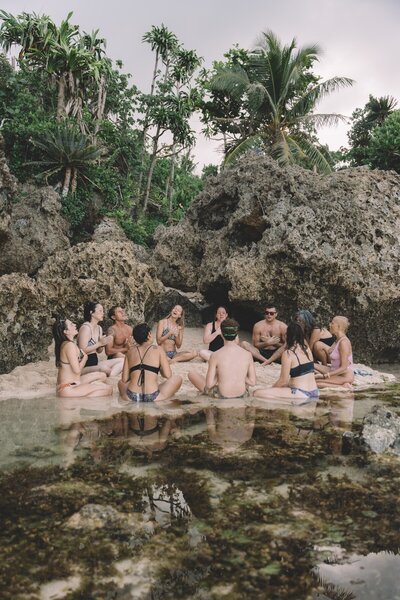 A group of people sit on the edge of the beach chanting mantras.
