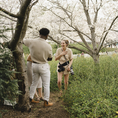 A photographer laughing with a couple standing on a small trail in a grassy area 