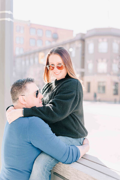 Husband stands behind wife with his arms around her.
