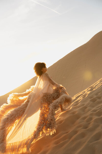 a woman in a huge dress running up a sand dune