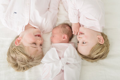 two-big-brothers-are-laying-down-and-looking-at-their-newborn-sister-for-their-newborn-family-portrait-session-with-nashville-family-and-newborn-photographer