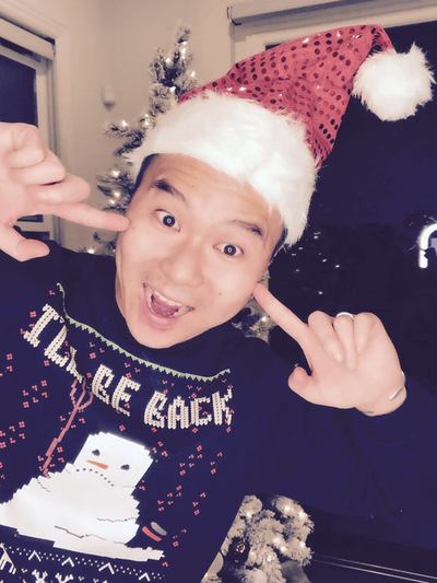 A person wearing a santa hat while pointing his cheeks and a big smile posing for a photo