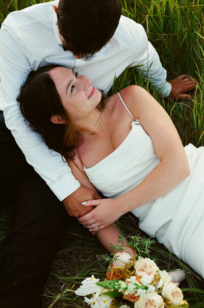 A bride and groom sit together in the grass, sharing a peaceful and intimate moment.