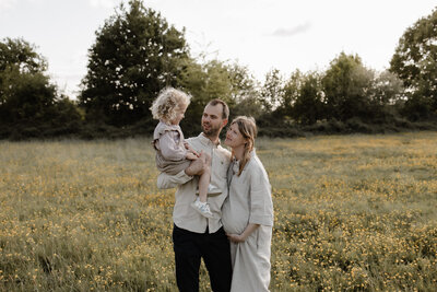 een papa en een zwangere mama kijken naar elkaar. hun oudste kindje zit in de nek van de papa. de foto werd genomen tijdens een fotoshoot in Bonheiden.