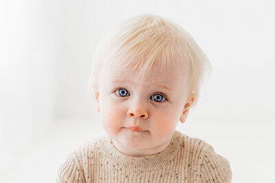 Baby girl blonde hair blue eyes wearing a beige romper