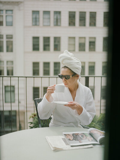 a stylish woman in a bathrobe and hair towel sips coffee in sunglasses on the balcony of Shinola Hotel in Detroit, Michigan