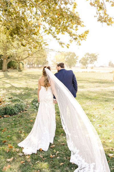 Bride and groom holding hands walking away from the camera as the bride's long veil flows behind them by Kansas City Wedding Photographer Sarah Riner Photography.