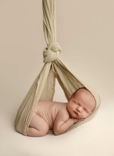 baby bundled up in a cream wrap, laying on their belly. Photo taken by Jenni Nikki Photography in Woodstock, GA