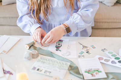 Elyse Stokes carefully styling a wedding invitation flatlay, selecting vintage stamps, silk ribbon colors, and ensuring a cohesive and beautiful aesthetic