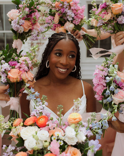 Joyful bridesmaid holding a vibrant bouquet of pink, orange, and white flowers, surrounded by friends, capturing the love and beauty of a Christ-centered celebration by Grace-Filled Gathering Co