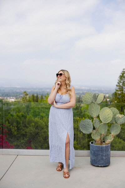 Brogan standing outside on a bright sunny day wearing sunglasses in a blue dress