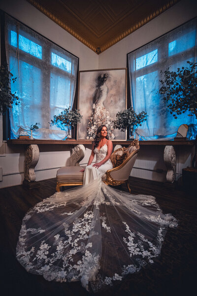 Bride sitting on a chaise sofa with floral veil displayed on the floor