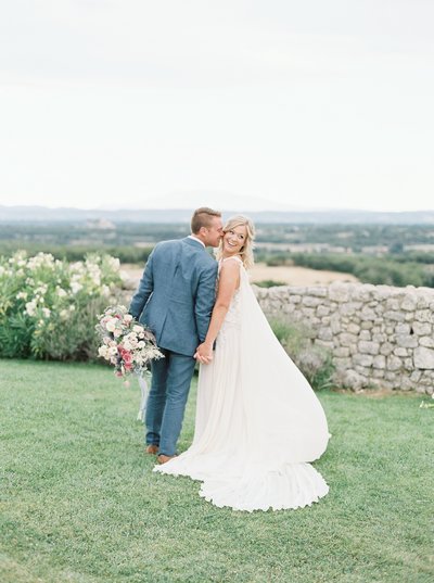 groom kissing bride on the cheek in front of a stone wall
