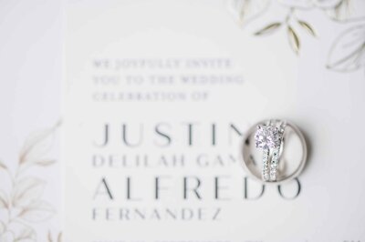 Detail shot of Bride and Groom wedding rings with wedding invitation in the background.