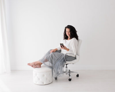 a portrait photographer sitting in a white chair and a all white background