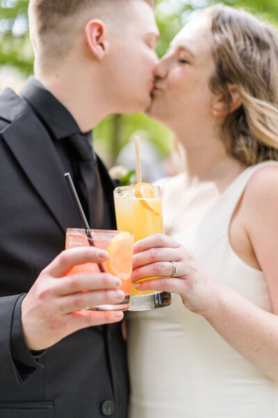 a couple kissing and clinking their drinks together at their park winters wedding.