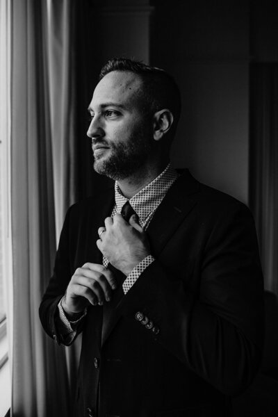 Groom adjusts his tie while looking out the window