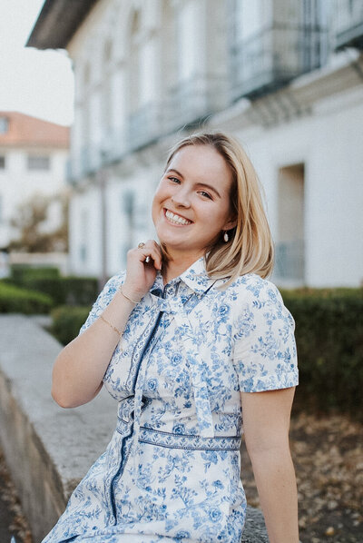 A portrait of the designer of Mia Munoz Design LLC. She is wearing a blue floral patterned dress with pearl jewelry.