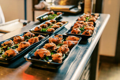 Multiple black trays of artfully plated appetizers arranged on a stainless steel counter in a restaurant kitchen, captured by Joseph Mayden for culinary marketing and brand content.