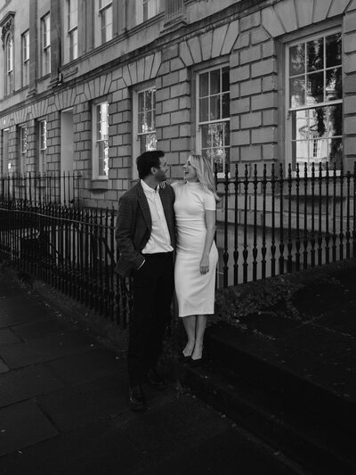 Black and white photo of man with his arms around pregnant woman's stomach while they kiss